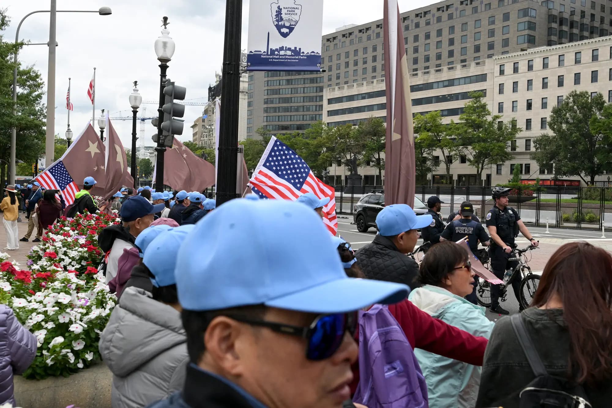 <em>Varias personas con banderas chinas y estadounidenses se encuentran cerca de agentes de policía que patrullan las inmediaciones del hotel Waldorf Astoria, mientras las calles y aceras de la zona permanecen cerradas al tráfico con motivo de la visita del líder chino Xi Jinping, en Washington, el 23 de septiembre de 2026. (Oliver Contreras/AFP vía Getty Images).</em>