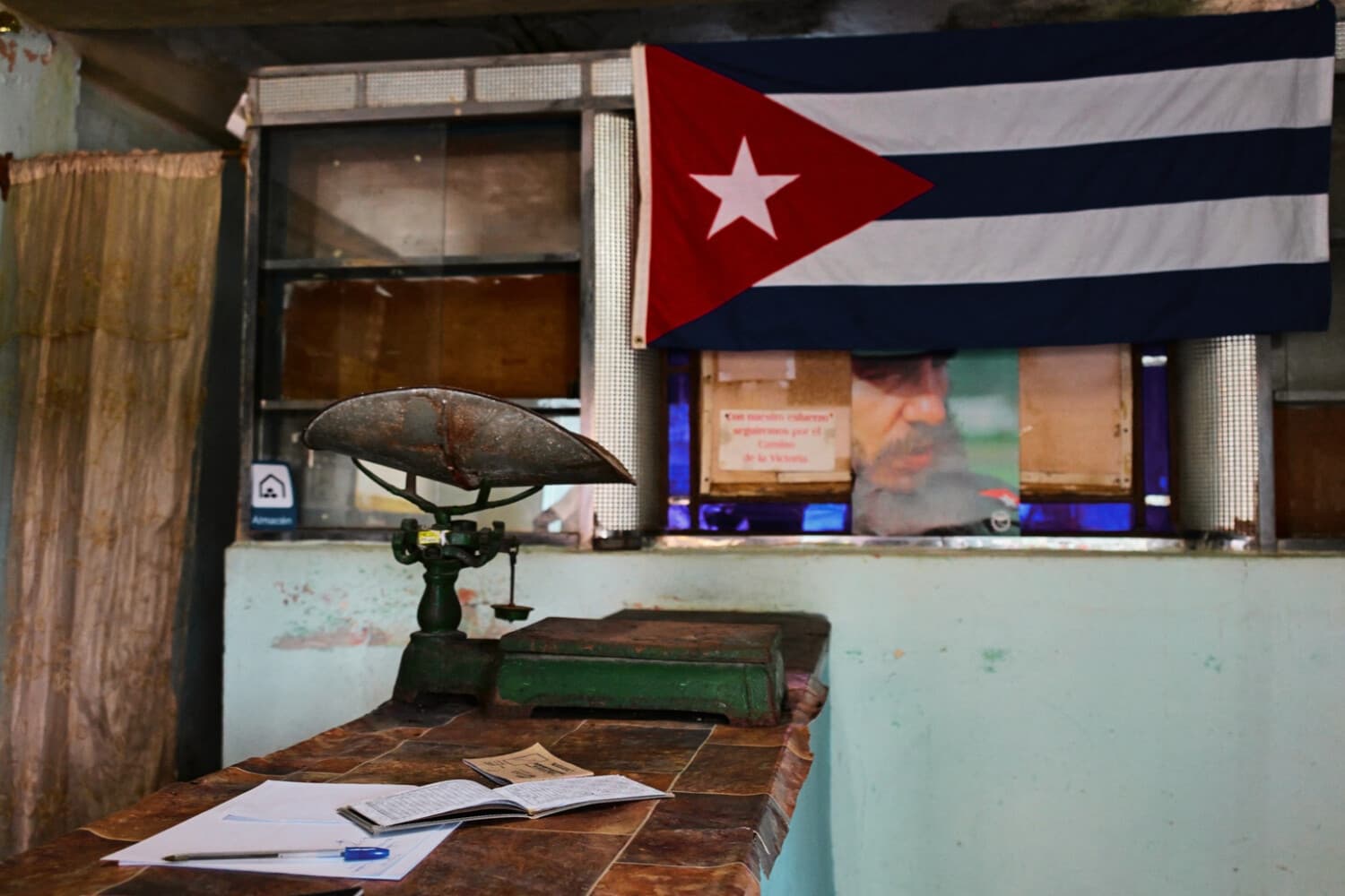 Una vieja balanza descansa sobre un mostrador, bajo una bandera cubana y un retrato del difunto líder cubano Fidel Castro, en el interior de una tienda de racionamiento —conocida localmente como «bodega»— en La Habana, el 5 de octubre de 2026. (YAMIL LAGE / AFP vía Getty Images)