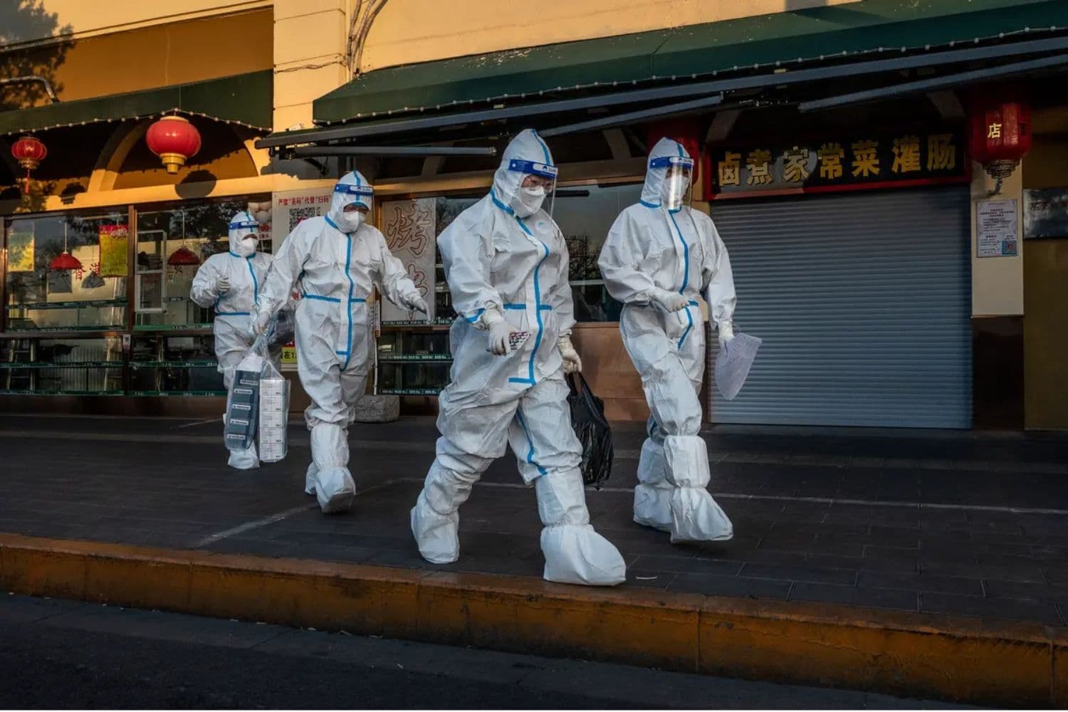 El 4 de diciembre de 2022, trabajadores de control de la pandemia pasan junto a una tienda cerrada cerca de una comunidad con residentes bajo monitoreo de salud por COVID-19 en Beijing. (Kevin Frayer/Getty Images)