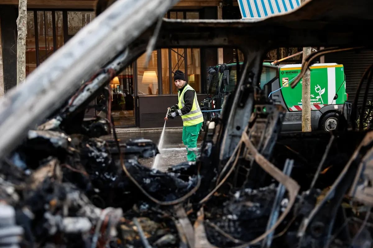 Un trabajador municipal, visto a través de un automóvil incendiado, limpia una calle un día después de los disturbios en París, Francia, el 18 de octubre de 2026. (Benoit Tessier/Reuters)