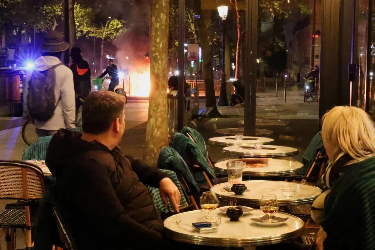 Los clientes de un café observan un incendio provocado por los alborotadores en París, Francia, el 17 de octubre de 2026. (Yann Tessier/Reuters)
