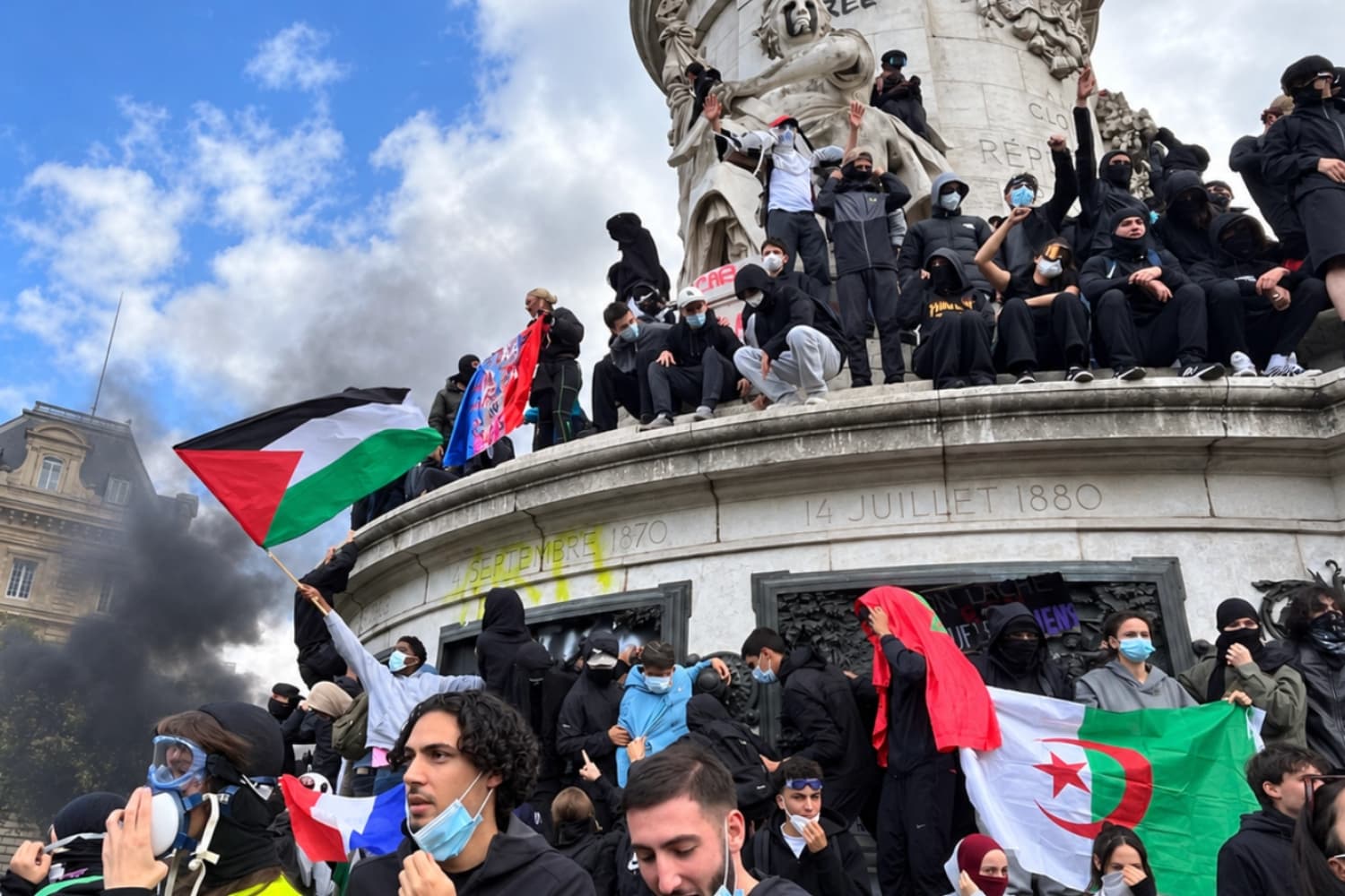 Manifestantes enmascarados en el Monumento a la República en la Plaza de la República de París durante las protestas de extrema izquierda del 17 de octubre de 2026. Se pueden ver banderas de Marruecos, Argelia y Palestina y una columna de humo negro.
(Etienne Fauchaire/The Epoch Times)
