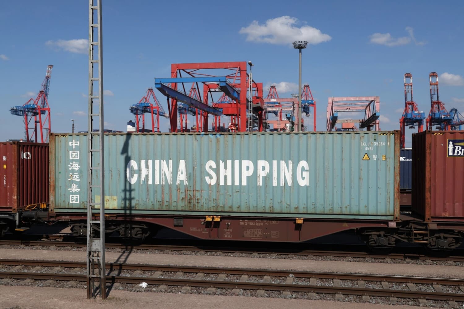 Contenedores de carga, incluido uno de China Shipping, yacen sobre vagones de plataforma, con grúas portuarias al fondo, en el puerto de Hamburgo, Alemania, el 15 de abril de 2025. (Sean Gallup/Getty Images)