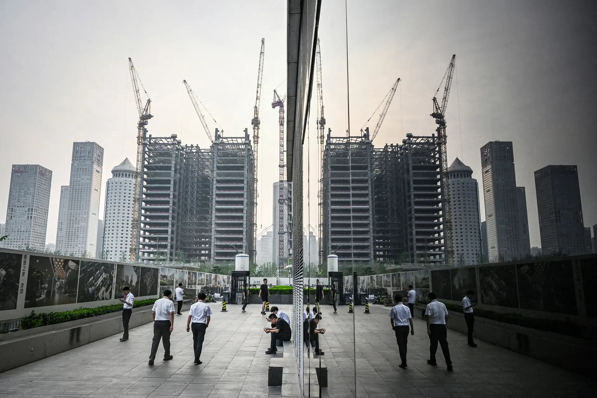 Empleados de oficina caminan junto al muro de una obra en el distrito financiero central de Beijing el 11 de julio de 2024. Los gobiernos locales de China controlan los terrenos urbanos y llevan mucho tiempo financiándose mediante la venta de derechos de urbanización. Esas ventas se han reducido drásticamente. (Greg Baker/AFP vía Getty Images)