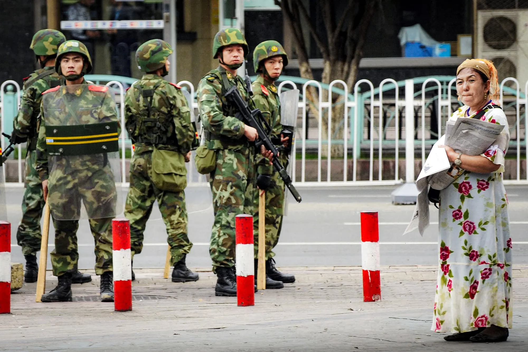 <em>Policías paramilitares chinos vigilan a una mujer de etnia uigur (derecha) mientras vende periódicos en el distrito uigur de la ciudad de Urumqi, en la región china de Xinjiang, el 14 de julio de 2009. (Peter Parks/AFP vía Getty Images).</em>