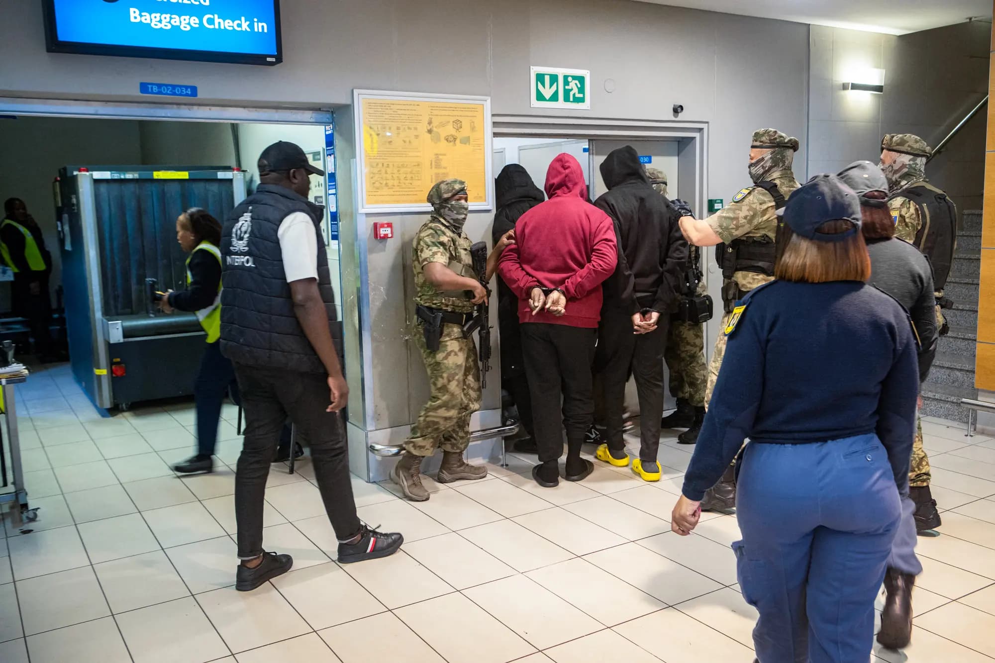 <em>Agentes de la Fuerza Especial de la Policía Sudafricana y de Interpol escoltan a seis ciudadanos nigerianos a través del Aeropuerto Internacional de Ciudad del Cabo tras ser extraditados a Estados Unidos para enfrentar cargos de estafas románticas en línea y lavado de dinero, en Ciudad del Cabo, Sudáfrica, el 11 de septiembre de 2026. (Rodger Bosch/AFP vía Getty Images).</em>