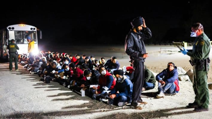 Inmigrantes ilegales esperan para abordar un autobús de la Patrulla Fronteriza de Estados Unidos para ser llevados a un centro de procesamiento después de cruzar la frontera desde México, en Yuma, Arizona, el 22 de mayo de 2022. (Mario Tama/Getty Images)