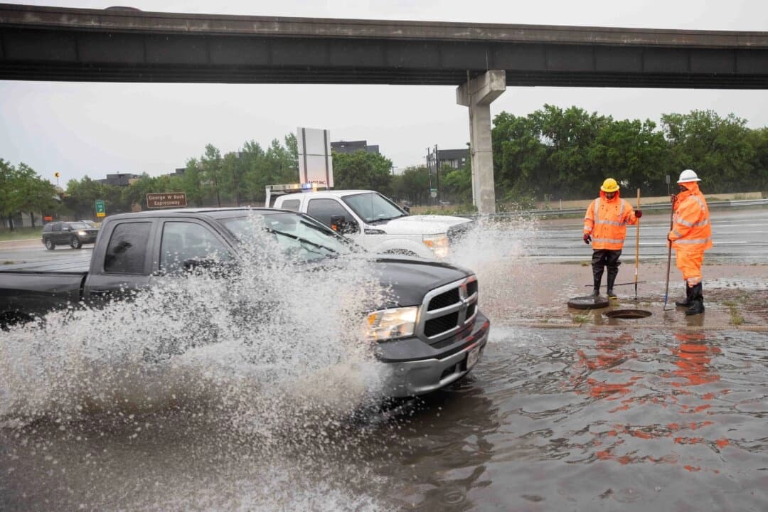 Una camioneta pasa mientras Tristan Neal y Kirk Jackson, del Departamento de Transporte de Texas (TxDOT), trabajan para desatascar una alcantarilla que provocó la inundación de la vía de servicio de la autopista N Central Expressway en Dallas el 30 de abril de 2025. (Juan Figueroa/The Dallas Morning News vía AP).