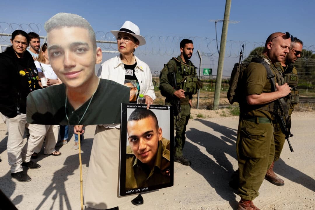 Varda Ben Baruch sostiene fotos de su nieto, el rehén israelí-estadounidense Edan Alexander, mientras camina cerca de soldados israelíes durante una manifestación de familiares de rehenes retenidos en la Franja de Gaza en Nir Oz, cerca de la frontera con la Franja de Gaza en Nir Oz, Israel, el 20 de abril de 2025. (Amir Levy/Getty Images)