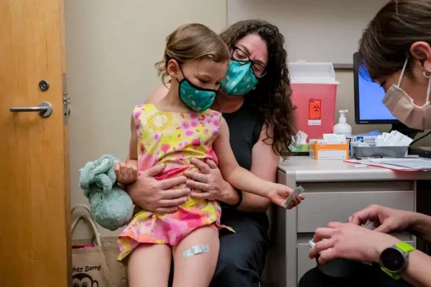 Una niña de 3 años sentada en el regazo de su madre en una foto de archivo durante una vacunación. (David Ryder/Getty Images)