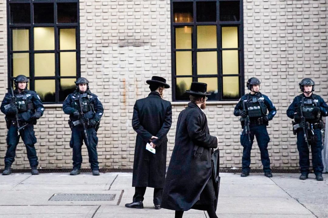 Hombres judíos ortodoxos pasan junto a la policía de Nueva York que custodia una sinagoga de Brooklyn antes del funeral de Mosche Deutsch, en la ciudad de Nueva York, el 11 de diciembre de 2019. (Mark Lennihan/AP Photo).