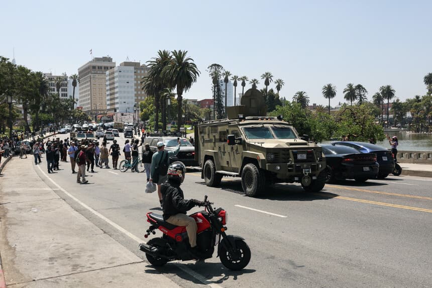 Los transeúntes observan cómo agentes de Aduanas y Protección Fronteriza circulan en vehículos blindados por Wilshire Boulevard, cerca de MacArthur Park, en Los Ángeles, el 7 de julio de 2025. (Patrick T. Fallon/AFP a través de Getty Images).