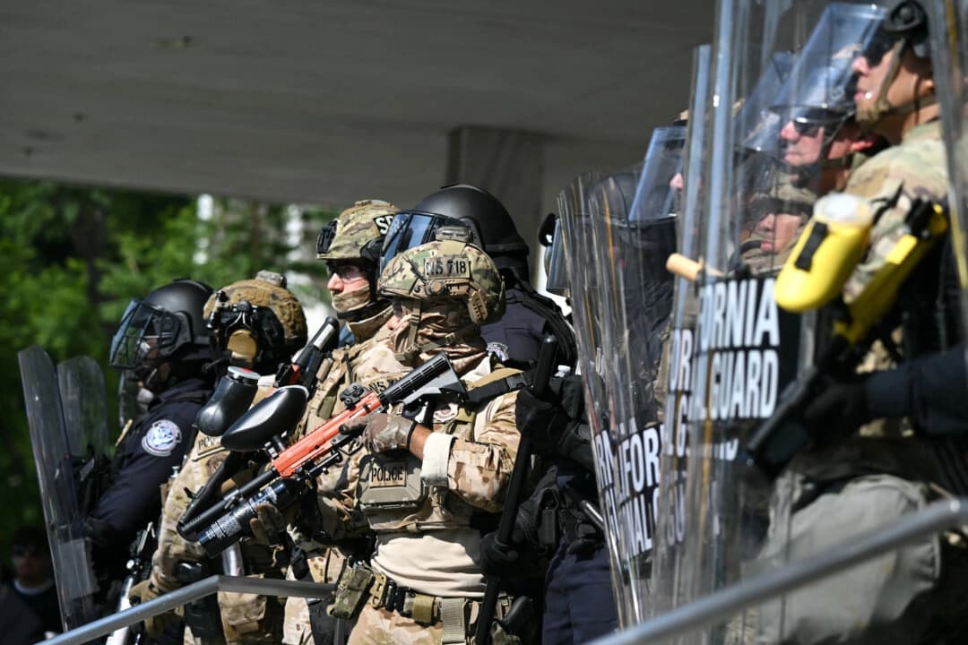 Agentes de policía flanqueados por miembros de la Guardia Nacional de California frente al edificio federal durante una protesta en respuesta a las operaciones federales de inmigración en Los Ángeles, el 9 de junio de 2025. (Ronaldo Schemidt/AFP a través de Getty Images)