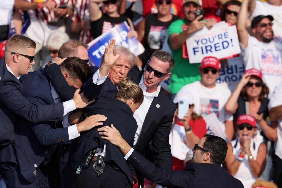 El entonces candidato presidencial Donald Trump hace un gesto con el rostro ensangrentado mientras es asistido por personal del Servicio Secreto después de recibir un disparo en la oreja derecha durante un mitin de campaña en el Butler Farm Show en Butler, Pensilvania, el 13 de julio de 2024. (Brendan McDermid/Reuters)