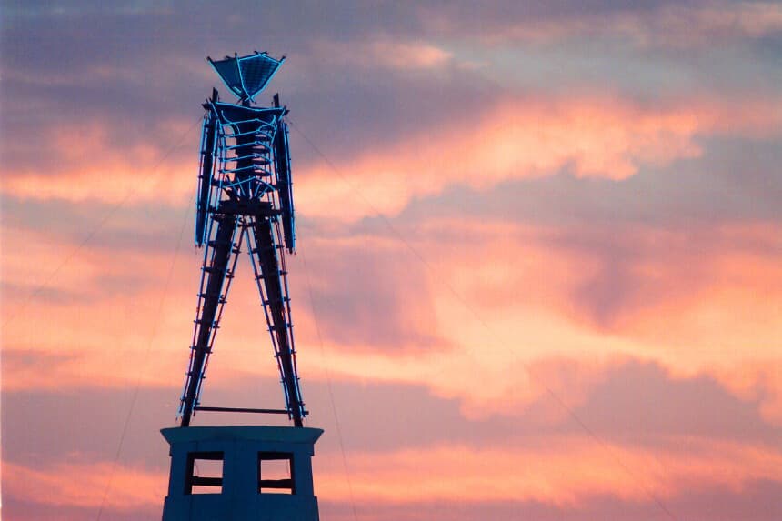 El sol sale detrás de una estatua de madera y neón, la pieza central del festival anual Burning Man, al norte de Gerlach, Nevada, el 26 de agosto de 2002. (Debra Reid/AP Photo).