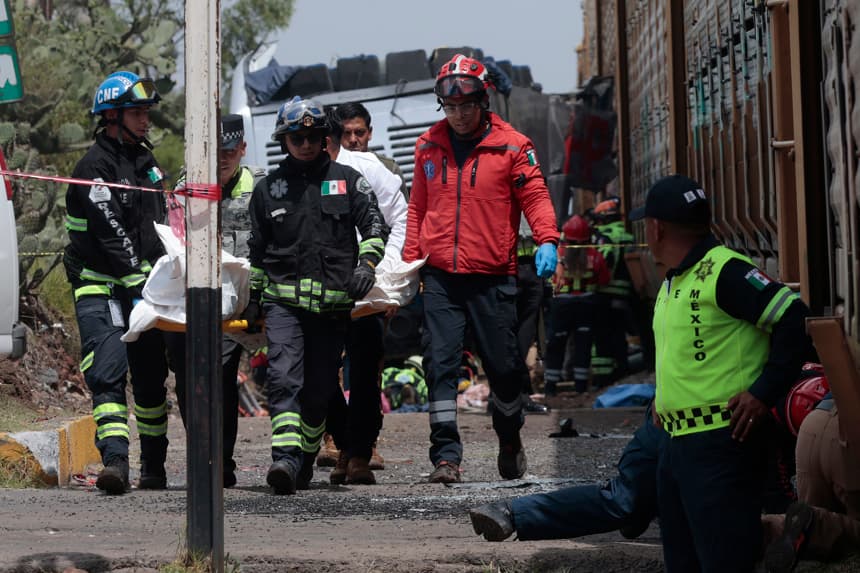 Integrantes de equipos de rescate trasladan el cuerpo de una persona, en la zona del accidente entre un ferrocarril y un autobús este lunes, en Atlacomulco, México. (EFE/Felipe Gutiérrez)