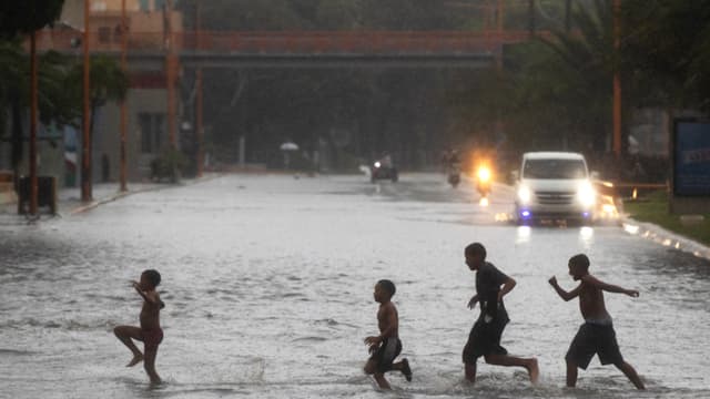 Un grupo de niños cruza por una calle inundada este jueves, en Santo Domingo, República Dominicana. (EFE/ Orlando Barría)