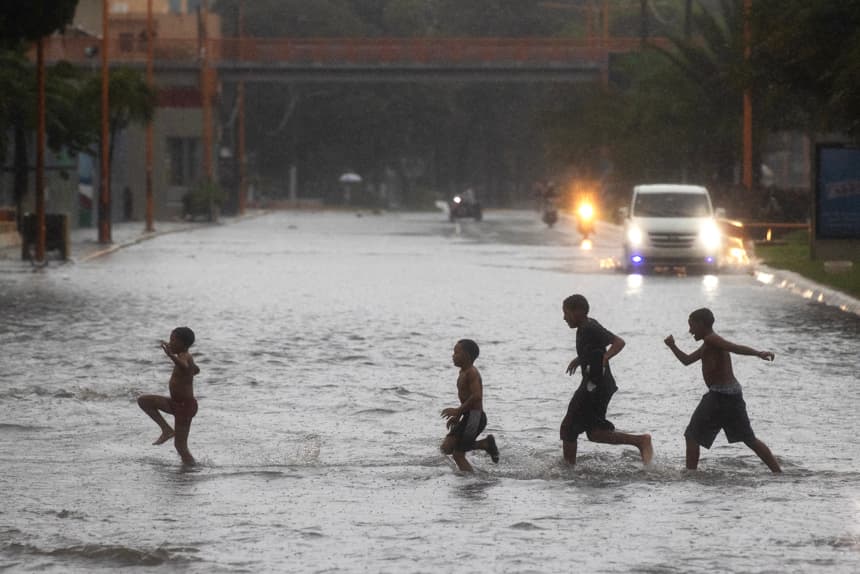 Un grupo de niños cruza por una calle inundada este jueves, en Santo Domingo, República Dominicana. (EFE/ Orlando Barría)