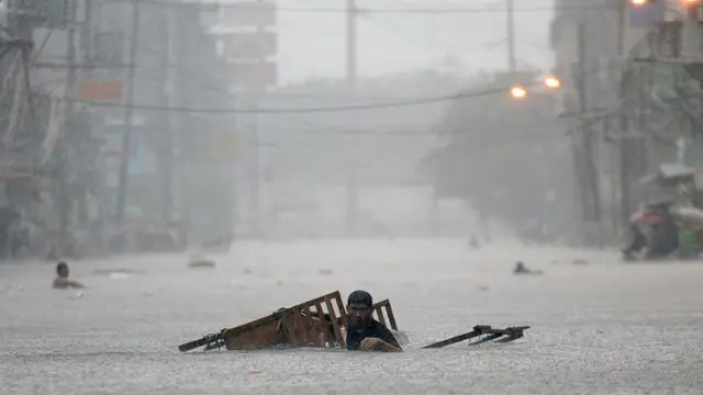 Un residente remolca su puesto ambulante mientras vadea una calle inundada durante las fuertes lluvias. Imagen de Archivo (TED ALJIBE/AFP a través de Getty Images)