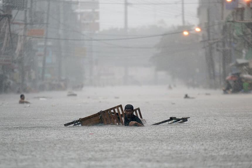 Un residente remolca su puesto ambulante mientras vadea una calle inundada durante las fuertes lluvias. Imagen de Archivo (TED ALJIBE/AFP a través de Getty Images)