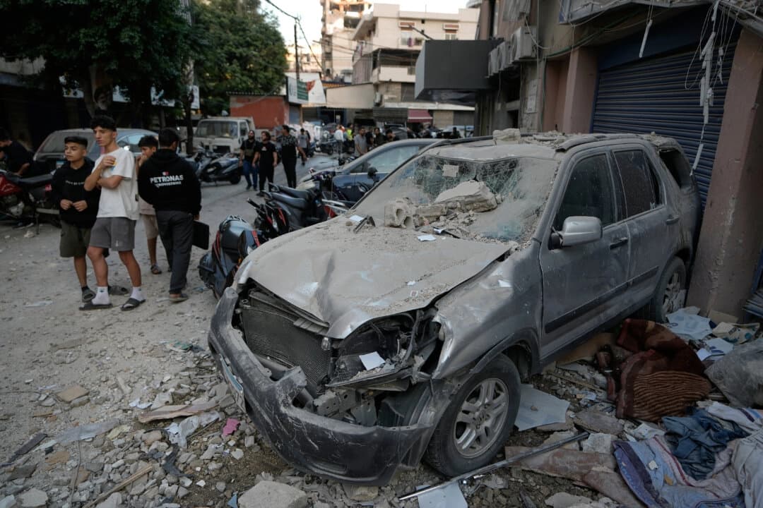 La gente pasa junto a un coche dañado en el lugar donde un ataque israelí alcanzó un edificio de apartamentos en Dahiyeh, en el suburbio sur de Beirut, el 23 de noviembre de 2025. Bilal Hussein/AP Photo