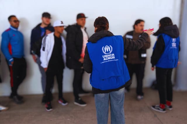 Solicitantes de asilo escuchan a los trabajadores del ACNUR en la entrada de la Comisión Mexicana de Ayuda a Refugiados y las oficinas del ACNUR en Tijuana, estado de Baja California, México, el 24 de enero de 2025. (Guillermo Arias/AFP a través de Getty Images)
