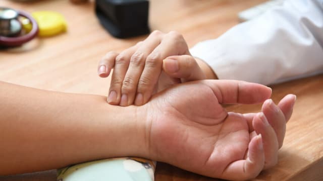 En esta foto tomada el 12 de octubre de 2017, la doctora singapurense Calista Lim Hui Min (derecha) toma el pulso a la paciente Elaine Low, de 35 años (izquierda), antes de recibir un masaje por parte de una masajista robot en la clínica de medicina tradicional china (MTC) NovaHealth de Singapur. Una robot masajista llamada Emma ofrece a los singapurenses masajes de alta tecnología con un gigantesco brazo metálico y puntas de silicona calientes que, según sus creadores, imitan a la perfección el tacto humano. El robot, creación de la startup local AiTreat, comenzó a trabajar esta semana en una clínica de la ciudad-estado y realiza "tui na", un tipo de masaje practicado en la medicina tradicional china. / AFP PHOTO / ROSLAN RAHMAN / PARA ACOMPAÑAR LA NOTICIA DE AFP SINGAPUR-TECNOLOGÍA-SALUD-EXCENTRICIDAD (El crédito de la foto debe leer ROSLAN RAHMAN/AFP a través de Getty Images).