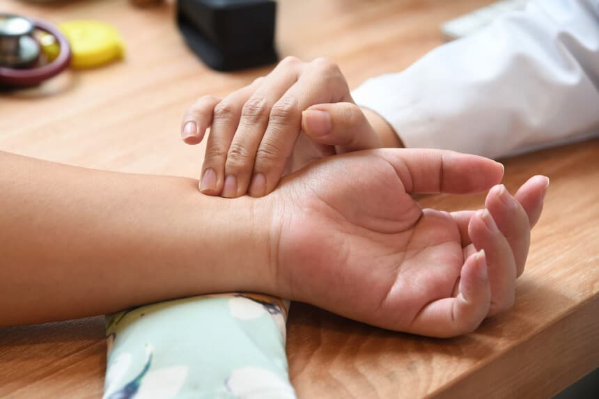 En esta foto tomada el 12 de octubre de 2017, la doctora singapurense Calista Lim Hui Min (derecha) toma el pulso a la paciente Elaine Low, de 35 años (izquierda), antes de recibir un masaje por parte de una masajista robot en la clínica de medicina tradicional china (MTC) NovaHealth de Singapur. Una robot masajista llamada Emma ofrece a los singapurenses masajes de alta tecnología con un gigantesco brazo metálico y puntas de silicona calientes que, según sus creadores, imitan a la perfección el tacto humano. El robot, creación de la startup local AiTreat, comenzó a trabajar esta semana en una clínica de la ciudad-estado y realiza "tui na", un tipo de masaje practicado en la medicina tradicional china. / AFP PHOTO / ROSLAN RAHMAN / PARA ACOMPAÑAR LA NOTICIA DE AFP SINGAPUR-TECNOLOGÍA-SALUD-EXCENTRICIDAD (El crédito de la foto debe leer ROSLAN RAHMAN/AFP a través de Getty Images).