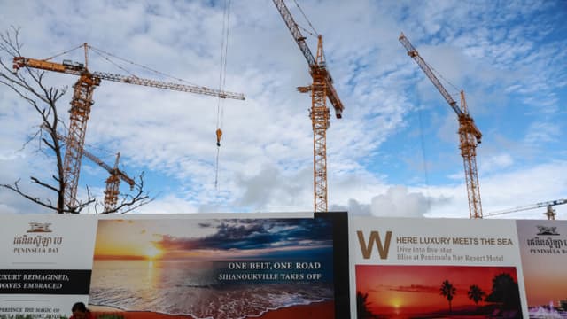 Una mujer sentada cerca de una valla publicitaria de la iniciativa china "El cinturón y la ruta" el 1 de julio de 2024 en Sihanoukville, Camboya. (Valeria Mongelli/Getty Images)