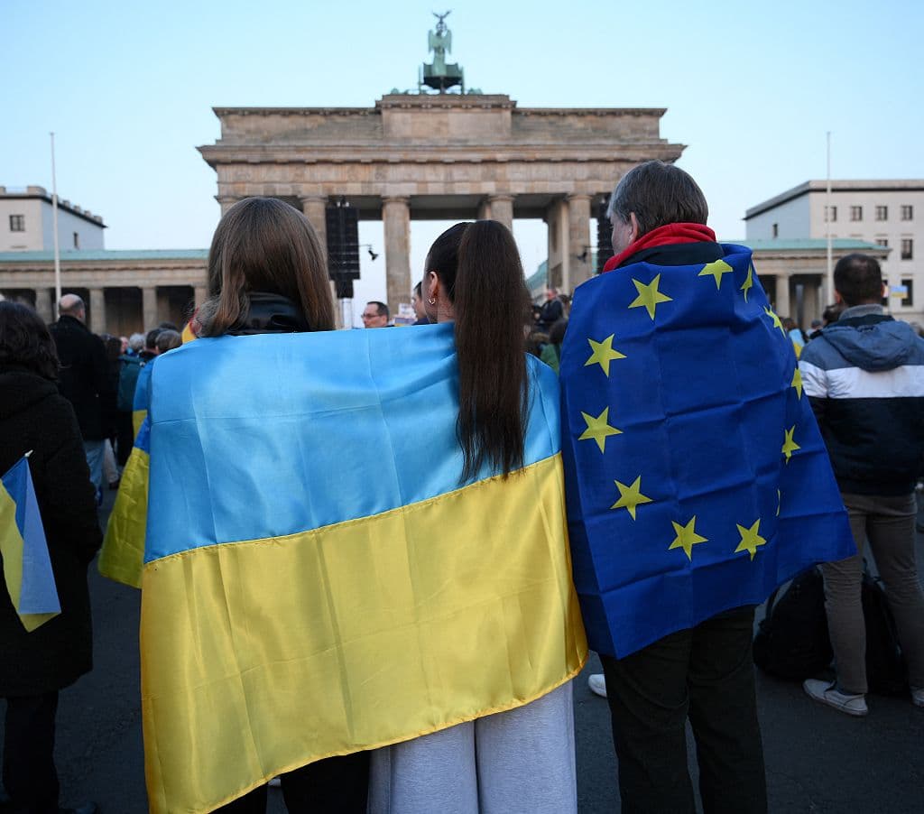 Un participante con la bandera europea (derecha) junto a unas jóvenes con la bandera ucraniana frente a la emblemática Puerta de Brandeburgo en Berlín, el 9 de marzo de 2025, durante una manifestación en apoyo a Ucrania. (Foto de RALF HIRSCHBERGER / AFP) (Foto de RALF HIRSCHBERGER/AFP a través de Getty Images)