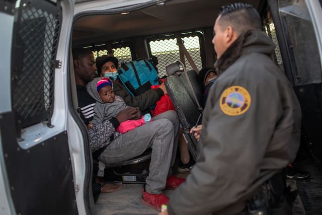 Inmigrantes de Haití y Venezuela esperan a ser trasladados por los ayudantes del sheriff a un centro de procesamiento de la Patrulla Fronteriza de los Estados Unidos el 11 de diciembre de 2021 en Yuma, Arizona. (Foto de John Moore/Getty Images)