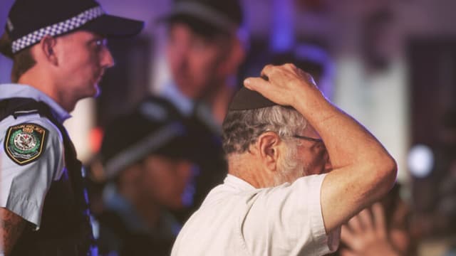 Un miembro de la comunidad judía reacciona mientras camina con la policía hacia el lugar del tiroteo en Bondi Beach, en Sídney, el 14 de diciembre de 2025. La policía australiana informó de que dos personas fueron detenidas tras recibir informes de múltiples disparos el 14 de diciembre en la famosa playa de Bondi Beach, en Sídney, e instó a la población a ponerse a cubierto. (DAVID GRAY / AFP a través de Getty Images)