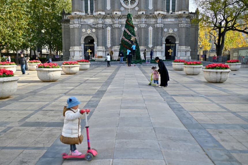 Wokers decorates a Christmas tree as children play in front of a church in Beijing on November 28, 2025. (Photo by WANG Zhao / AFP via Getty Images)