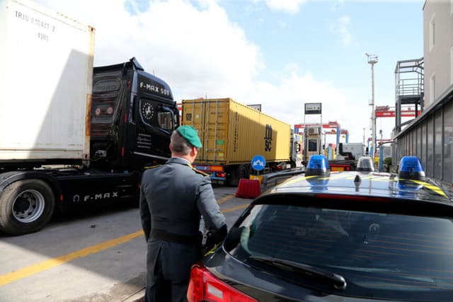 Un agente de la Guardia di Finanza, la policía italiana encargada de los delitos financieros y el contrabando, revisa camiones que transportan contenedores en la zona comercial del puerto de Nápoles, el 29 de febrero de 2024. (CARLO HERMANN/AFP vía Getty Images)