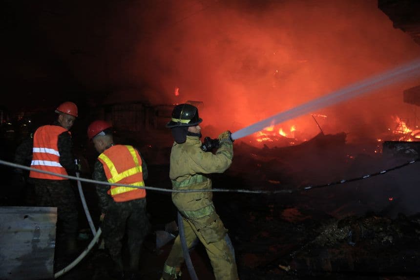 Un integrante del Cuerpo de Bomberos de Honduras sostiene utiliza una manguera para controlar el fuego durante un incendio provocado en un puesto de venta de pólvora este lunes, en el mercado Medina Concepción de San Pedro Sula, Honduras. (EFE/ José Valle)