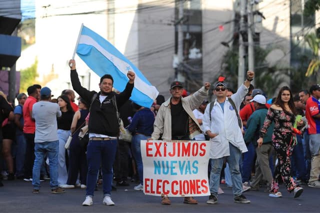 Personas sostienen carteles y banderas frente al Congreso Nacional durante una sesión extraordinaria en Tegucigalpa, Honduras. EFE/ Gustavo Amador
