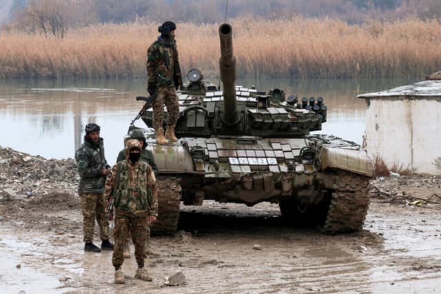 Personal militar se encuentra en el cruce que conecta las dos orillas del río Éufrates, mientras otras personas intentan cruzar al otro lado después de que las Fuerzas Democráticas Sirias (SDF) se retiraran de la provincia de Deir al-Zor y el ejército sirio tomara el control total de la zona, en Deir al-Zor, Siria, el 18 de enero de 2026. (Khalil Ashawi/Reuters).