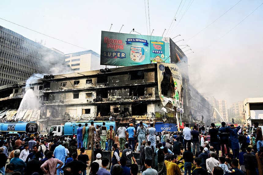 La gente observa cómo los bomberos realizan una operación de enfriamiento en una estructura quemada tras un gran incendio en un centro comercial de Karachi el 19 de enero de 2026. (Asif HASSAN / AFP vía Getty Images)