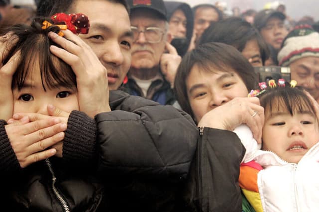 Un padre y una madre tapan los oídos de sus hijos para protegerlos del ruido de los petardos durante las celebraciones del Año Nuevo chino, el 9 de febrero de 2005, en el barrio de Chinatown de la ciudad de Nueva York. El Año Nuevo Lunar chino de este año celebra el Año del Gallo. (Foto de Stephen Chernin/Getty Images).