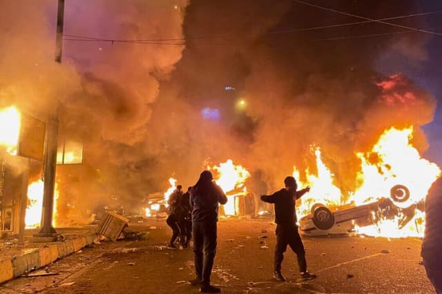Manifestantes iraníes se reúnen alrededor de coches en llamas mientras bloquean una calle durante una protesta en Teherán, Irán, el 8 de enero de 2026. (Aghasht/Middle East Images/AFP a través de Getty Images).
