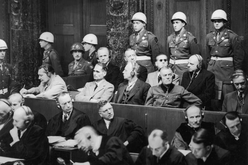 22 de noviembre de 1945: Miembros del Tercer Reich de Adolf Hitler sentados en el estrado con auriculares puestos, en el tercer día del juicio por crímenes de guerra del Tribunal Militar Internacional en Núremberg, Alemania. De izquierda a derecha (primera fila): Hermann Goering (escribiendo), Rudolf Hess, Joachim von Ribbentrop y Wilhelm Keitel; (segunda fila) Karl Donitz, Erich Raeder, Baldur von Schirach y Fritz Sauckel. La policía militar se encuentra detrás de ellos. (Hulton Archive/Getty Images)
