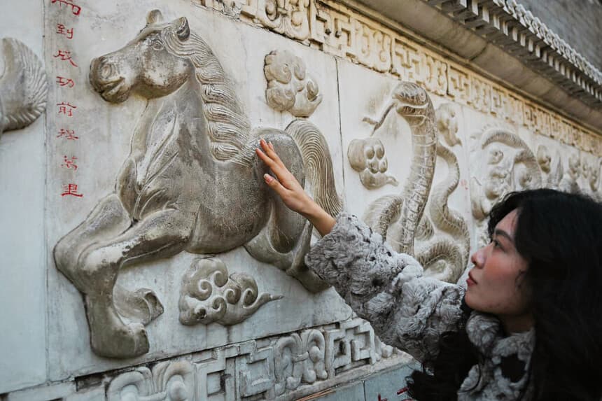Una mujer toca una figura de caballo en un muro de piedra que representa animales del zodíaco chino en un templo de Beijing el 12 de febrero de 2026, antes del Año Nuevo Lunar del Caballo. (Pedro PARDO / AFP vía Getty Images)