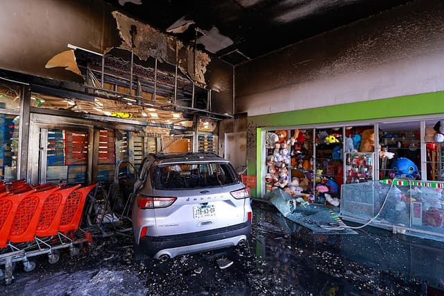 Un coche quemado se estrella contra la entrada de una tienda en un centro comercial el 22 de febrero de 2026 en Guadalajara, México. (Carlos Zepeda/Getty Images)