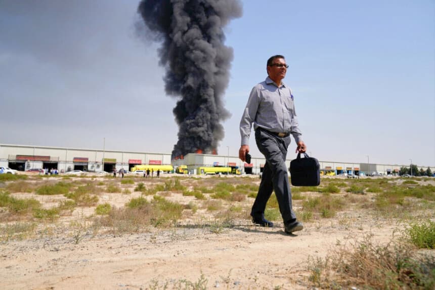 Un hombre se aleja mientras una columna de humo negro se eleva desde un almacén en la zona industrial de la ciudad de Sharjah, Emiratos Árabes Unidos, tras las noticias de ataques iraníes en Dubái, el 1 de marzo de 2026. (Altaf Qadri/AP Photo).