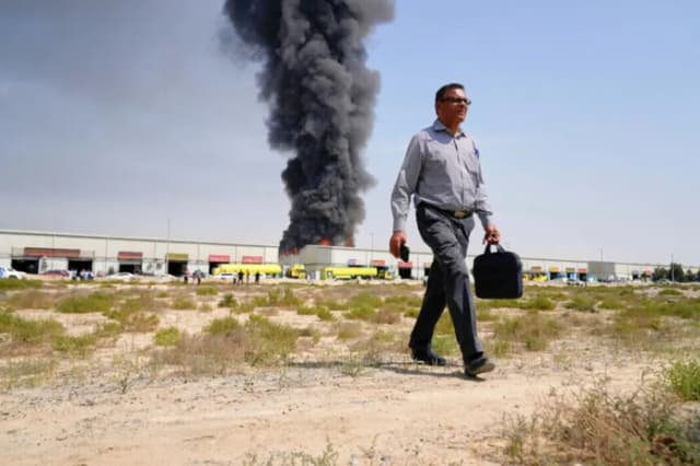 Un hombre se aleja mientras una columna de humo negro se eleva desde un almacén en la zona industrial de la ciudad de Sharjah, Emiratos Árabes Unidos, tras las noticias de ataques iraníes en Dubái, el 1 de marzo de 2026. (Altaf Qadri/AP).