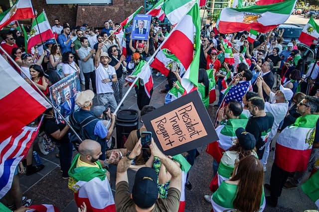 Una mujer sostiene una foto de Reza Pahlavi, hijo del antiguo Sha de Irán, mientras la gente ondea banderas estadounidenses e iraníes anteriores a la Revolución Islámica de 1979 y baila con miembros de la comunidad iraní en Los Ángeles, el 28 de febrero de 2026. (Apu GOMES / AFP a través de Getty Images)
