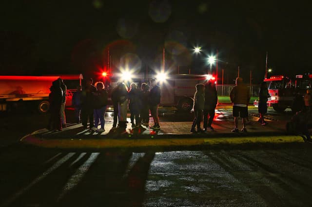 Varias personas se encuentran junto a los vehículos de los bomberos en una imagen ilustrativa. (Julio César AGUILAR / AFP vía Getty Images)