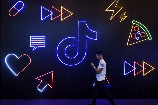 Un hombre que sostiene un teléfono pasa junto a un cartel de la aplicación TikTok de la empresa china ByteDance, conocida localmente como Douyin, en la Exposición Internacional de Productos Artificiales en Hangzhou, provincia de Zhejiang, China, el 18 de octubre de 2019. (STR/Archivos/Reuters)