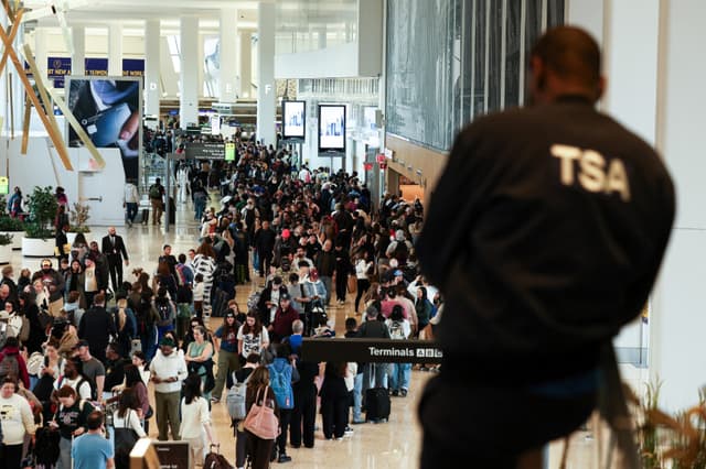 Un agente de la Administración de Seguridad en el Transporte (TSA) observa a los pasajeros que hacen cola para pasar el control de seguridad en el aeropuerto LaGuardia de Nueva York el 22 de marzo de 2026. A partir del 23 de marzo se desplegarán agentes de inmigración en los aeropuertos estadounidenses con el objetivo de aliviar la creciente congestión en los controles de seguridad, en medio de un enfrentamiento presupuestario que dura ya varias semanas y que gira en torno a la campaña de deportaciones masivas del presidente Donald Trump, según informaron las autoridades. Trump anunció esta medida extraordinaria en una publicación en las redes sociales el domingo por la mañana, lo que llevó a las autoridades a ponerse manos a la obra para elaborar rápidamente un plan. (Foto de CHARLY TRIBALLEAU / AFP vía Getty Images).