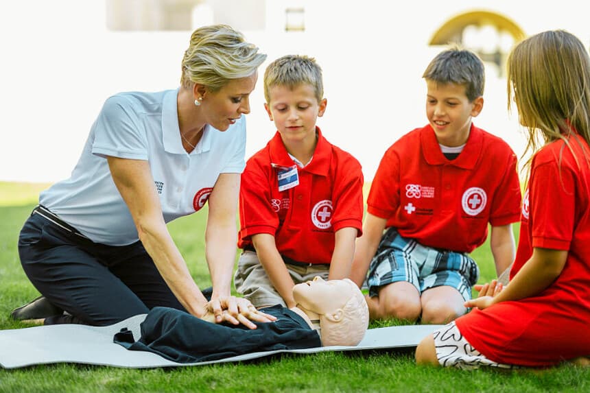 La princesa Charlene de Mónaco (izquierda), embajadora de buena voluntad de la Federación Internacional de Sociedades de la Cruz Roja y de la Media Luna Roja (FICR), muestra a unos niños cómo realizar compresiones torácicas durante la presentación del Día Mundial de los Primeros Auxilios 2016, el 9 de septiembre de 2016 en la Oficina de las Naciones Unidas en Ginebra. (FABRICE COFFRINI / AFP vía Getty Images)